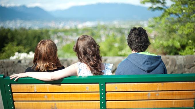 Three people sitting on a bench looking at a view of hills