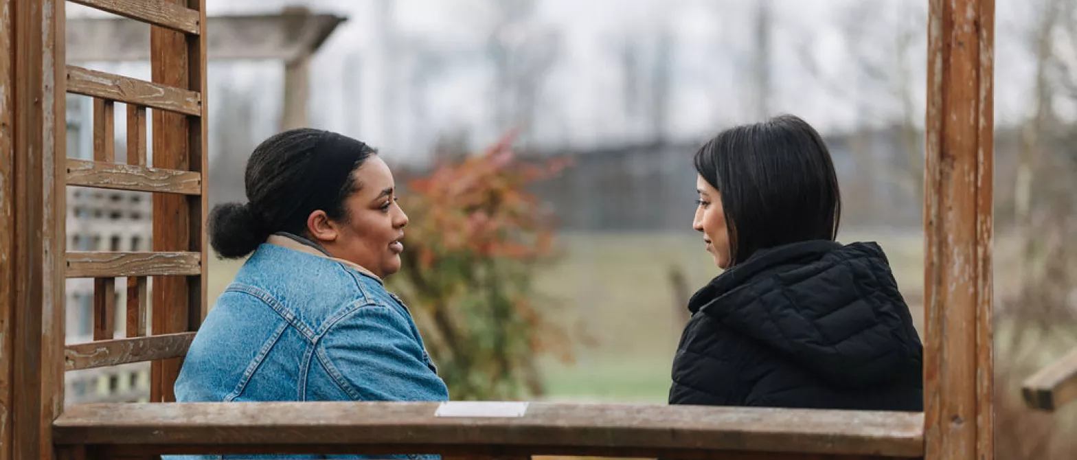 Two women sitting on a bench outside and talking