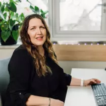 Woman with long brown hairs sits at a desk with a computer keyboard in front of her.