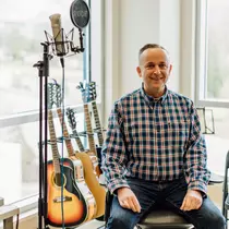 Man sits in front of a rack of guitars.