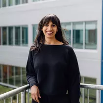 A woman stands on a balcony and smiles at the camera.