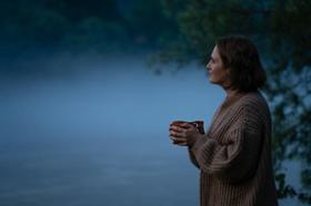 Woman gazing outwards at dusk while holding mug