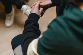 Person's clasped hands as they lean forward in conversation