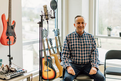 Man sits in front of a rack of guitars.