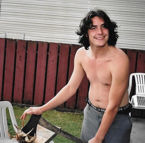 Shirtless man with wavy black hair holds an axe against a small crab.